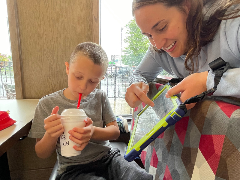 Katie having a AAC speech therapy session with a boy while drinking his milkshake at a Chik Fil A Restaurant with his AAC device